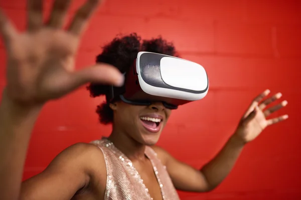 Cool millennial black woman exploring space with virtual reality glasses by a red concrete wall Stock Photo