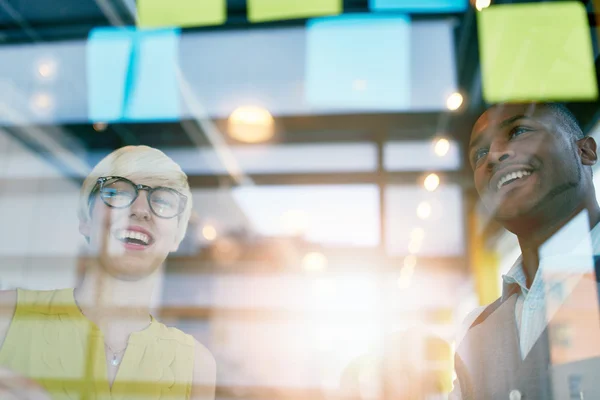 Dos propietarios de pequeñas empresas milenarias creativas que trabajan en una lluvia de ideas de estrategia de redes sociales utilizando notas adhesivas en ventanas — Foto de Stock