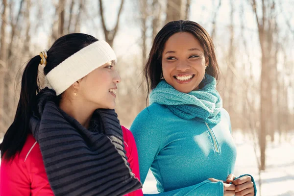 Multi-ethnic pair of female friends taking a break from jogging in the snow in winter — Stock Photo, Image