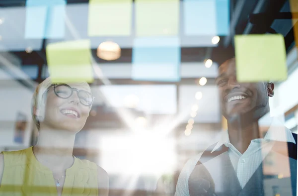 Dos propietarios de pequeñas empresas milenarias creativas que trabajan en una lluvia de ideas de estrategia de redes sociales utilizando notas adhesivas en ventanas — Foto de Stock