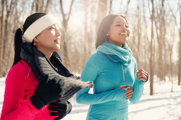 Multi-ethnic pair of female friends taking a break from jogging in the snow in winter — Stock Photo, Image