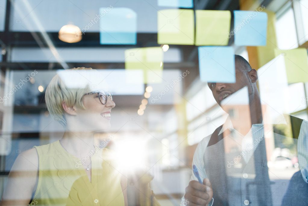 Two creative millenial small business owners working on social media strategy brainstorming using adhesive notes in windows