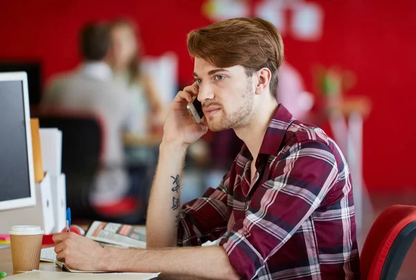 Αυτοπεποίθηση αρσενικό σχεδιαστής μιλώντας σε ένα κινητό τηλέφωνο σε κόκκινο δημιουργικών γραφείων — Φωτογραφία Αρχείου