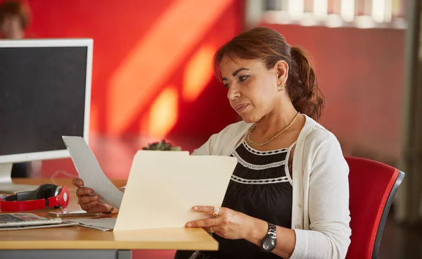 Diseñadora femenina segura trabajando y revisando documentos dentro de una carpeta en un espacio de oficina creativo rojo — Foto de Stock
