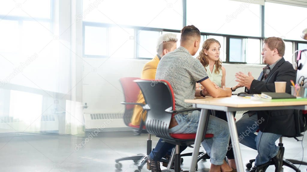 Unposed group of creative business entrepreneurs in an open concept office brainstorming together on a digital tablet.