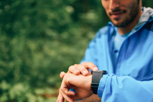 Sprawny mężczyzna jogger dzień za pomocą zegarka smartwatch podczas Krzyż kraju lasu szlak wyścigu w parku przyrody. — Zdjęcie stockowe