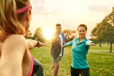 Çeşitli ve karışık cinsiyet fitness sınıfı günbatımında doğa parkında egzersiz