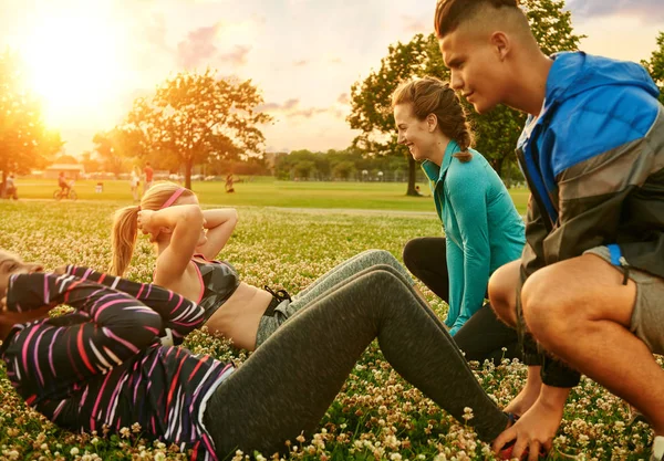 Grupo diverso de millenials durante a aula de fitness fazendo sit-ups ao pôr do sol no parque da natureza — Fotografia de Stock