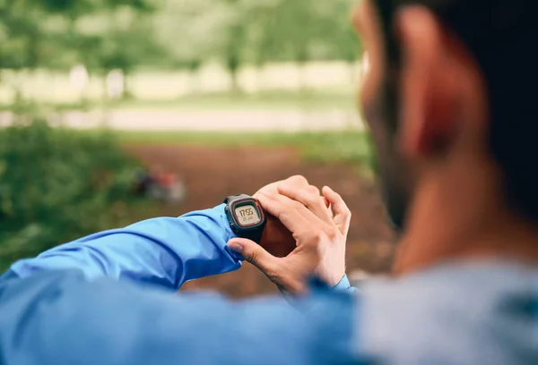 Çapraz ülke orman iz yarış sırasında bir smartwatch bir doğa parkında kullanarak uygun erkek koşucu gün. — Stok fotoğraf