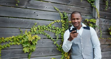 Yakışıklı siyah adam dışarı asılı, ahşap bir çit yanında dışında onun hareket eden smartphone ile mesaj