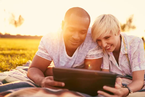 Coppia di razza mista di millennial in un campo di erba guardando un tablet digitale e leggendo per il loro prossimo giornale scolastico — Foto Stock