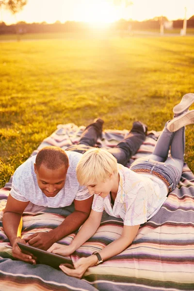 Coppia di razza mista di millennial in un campo di erba guardando un tablet digitale e leggendo per il loro prossimo giornale scolastico — Foto Stock