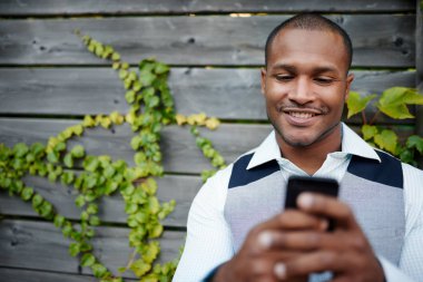 Yakışıklı siyah adam dışarı asılı, ahşap bir çit yanında dışında onun hareket eden smartphone ile mesaj