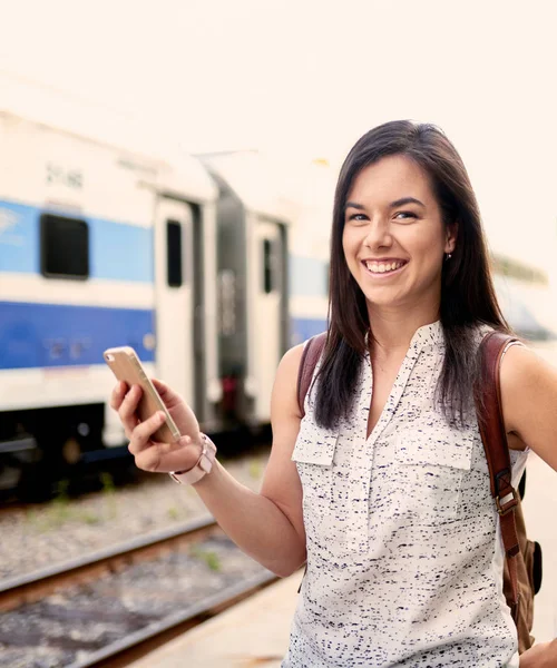 Studente millenaria fiduciosa in movimento controllando il suo smartphone su una piattaforma del treno — Foto Stock