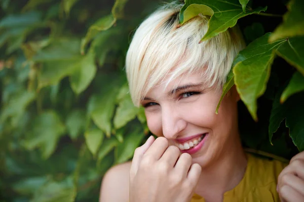 Vackra korthårig platina blond kvinna stående mot en murgröna staket bakgrund — Stockfoto