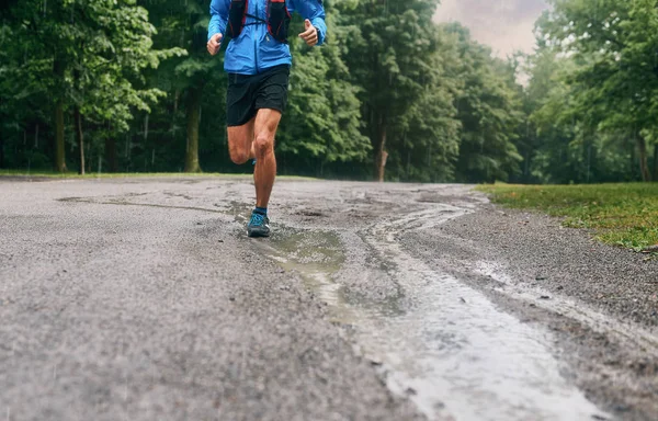 Terneros musculares de entrenamiento de jogger masculino en forma para la carrera de senderos forestales a campo traviesa bajo la lluvia en un sendero natural . — Foto de Stock