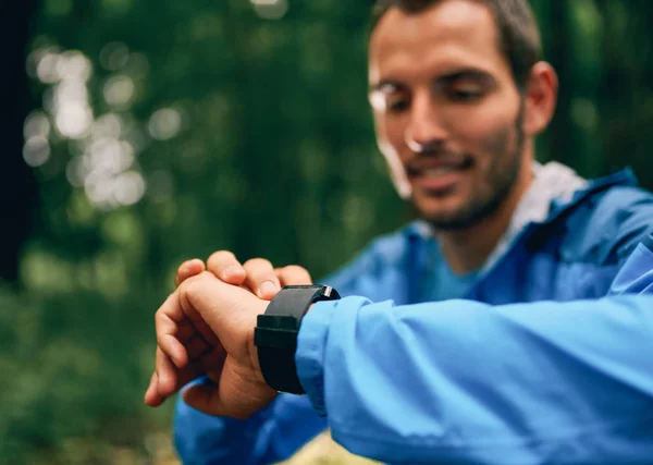 Ajuste el día del corredor masculino usando un reloj inteligente durante la carrera de senderos forestales de cross country en un parque natural . — Foto de Stock