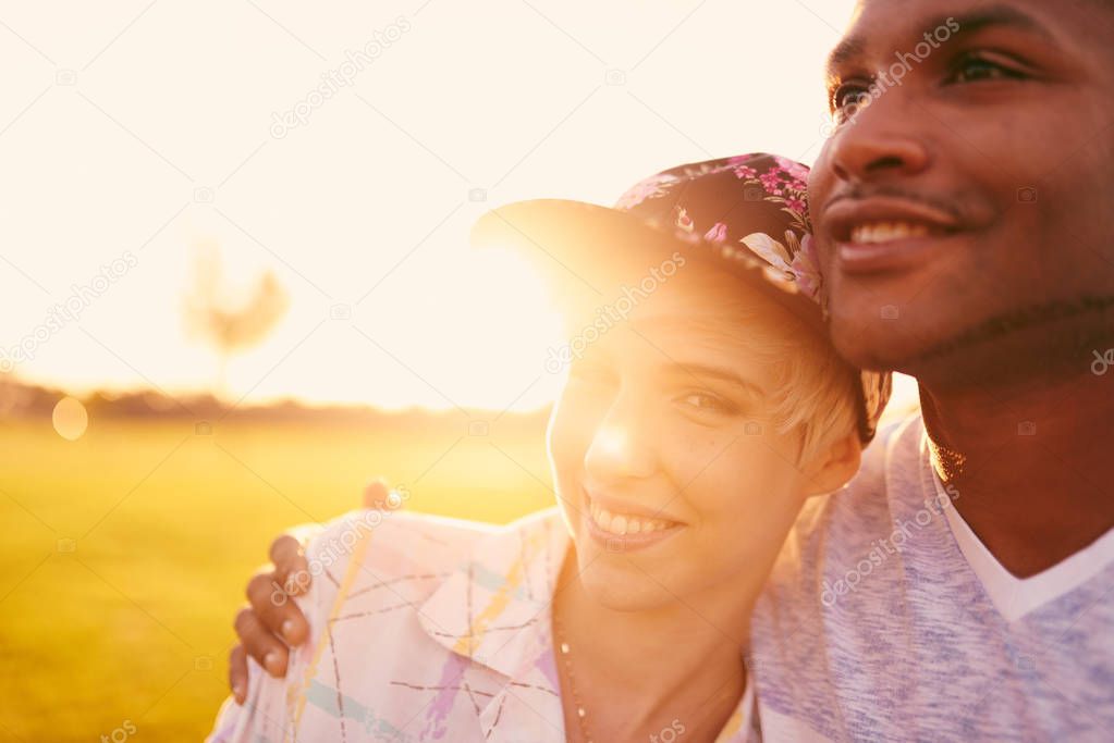 Mixed race couple of millennials in a grass field cuddling and showing affection together