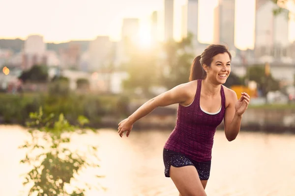 Porträtt av aktiva millenial kvinna jogging i skymningen med urbana stadsbilden och solnedgången i bakgrunden — Stockfoto