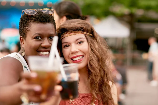 Diverse group of two girls having a drink in the crowd of a summer music festival — Stock Photo, Image