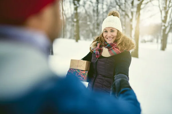 Фотография разношерстной пары, держащей рождественские подарки во время прогулки по зимнему лесу — стоковое фото