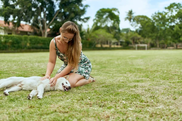 Young, beautiful blonde girl playing outdoors with friendly pupp Stock Image