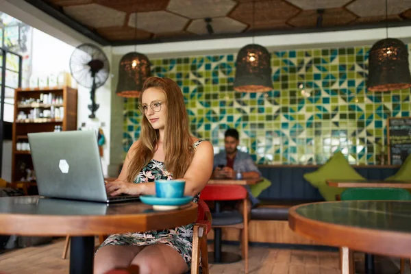 Mooie millennial vrouw typen op laptop zitten aan tafel in Rechtenvrije Stockfoto's