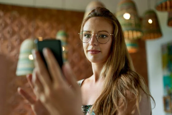 Gözlüklü güzel bir milenyum kadını video için akıllı telefon kullanıyor. Stok Resim