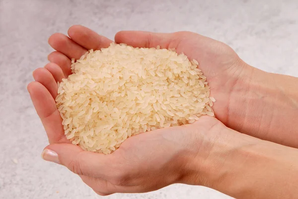 Algum arroz cru está em mãos femininas, um punhado de arroz branco — Fotografia de Stock