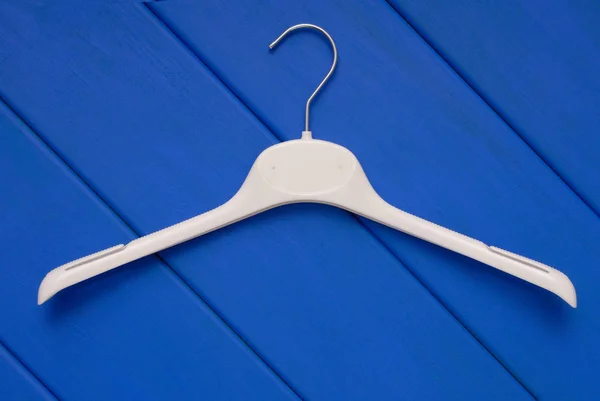 White coat-hanger, plastic clothes-hanger is on blue wooden back — Stock Photo, Image