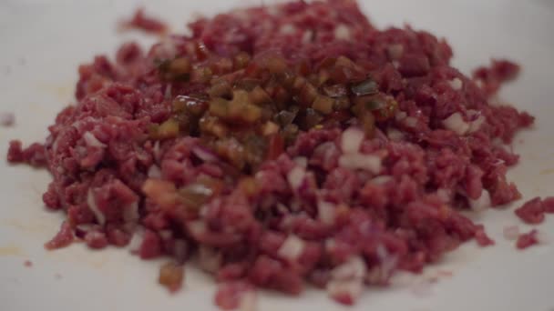 Close up of cooking meat tartare in slow motion. Cucumber slices mixing with chopped meat with forks. — Stock Video