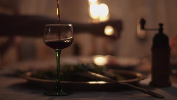 Flüssigkeit im Glas mit verschwommenem Abendessen mit Kerzenlicht auf dem Hintergrund. Hände nehmen Speisen und Getränke in Zeitlupe. — Stockvideo