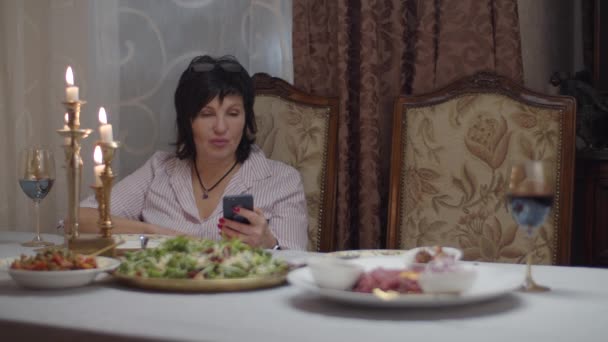 Brunette adult women sitting alone at the dinner table and surfing online in smartphone while waiting for friend for have lunch with wine in slow motion. — Stock Video