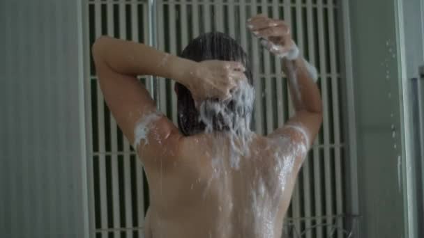 Brunetky se sprchují a pomalu si myjí vlasy šamponem. Zadní strana mladé třicátnice ve sprše. — Stock video