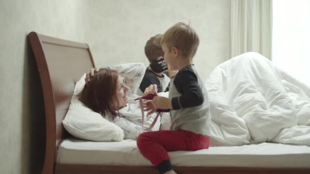 Dos hermanos en el mismo pijama llegando a la madre dormida con máscara en cámara lenta. Hijos molestando a la madre por la mañana. Familia jugando en la cama . — Vídeos de Stock