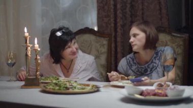 Esmer, yetişkin bir anne, kızının internette sörf yapmasını engellerken klasik bir şekilde şarapla yemek yiyor. Kadınlar gülüyor. 