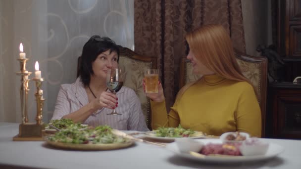 Brunett vuxna kvinnor med hennes röda hår vän äter middag med vin i slow motion. Kvinnliga vänner pratar och äter i klassisk interiör med ljus. — Stockvideo