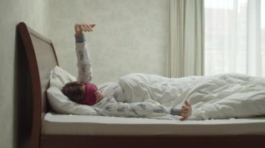 Parlak pijamaları ve uyku maskesiyle gülümseyen genç esmer kadın yatak odasında ağır çekimde uyanıyor. Kadınlar sabah yatakta eğleniyor.. 