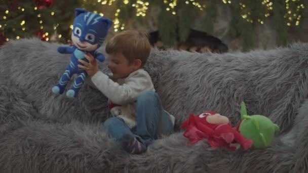 Véspera de Ano Novo, menino brincando com brinquedos macios PJ Máscaras no sofá . — Vídeo de Stock