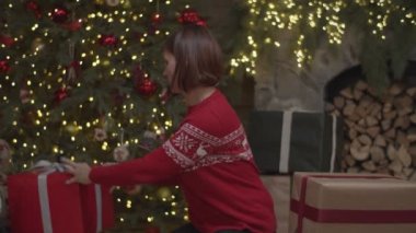 Kırmızı kazaklı esmer kadın Noel hediyelerini yavaş çekimde Noel ağacına sarıyordu. Kadınlar yılbaşı hediyelerinde yavaş çekimde isimler yazarlar.. 