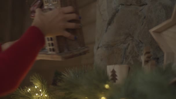 Kobieta umieszczenie zabawki dom Bożego Narodzenia na ozdobione światła kominek w zwolnionym tempie. — Wideo stockowe