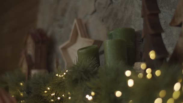 Kadın eli yeşil mumları takıyor. Işıklarla süslenmiş. Noel şöminesi yavaş çekimde.. — Stok video