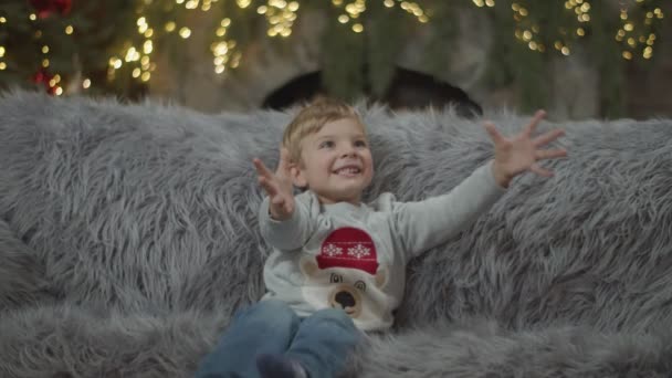 Дитячий хлопчик грає з м'якою іграшкою цуценяти на сірому дивані в різдвяній прикрасі в повільному русі. Хлопчик кидає і ловить грубу іграшку . — стокове відео