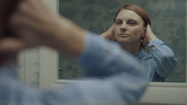 Bruneta dospělá žena v modré košili obdivuje svůj odraz v zrcadle ve zpomaleném filmu. Šťastné ženy dotýkají vlasy a usmívají se na její odraz. — Stock video