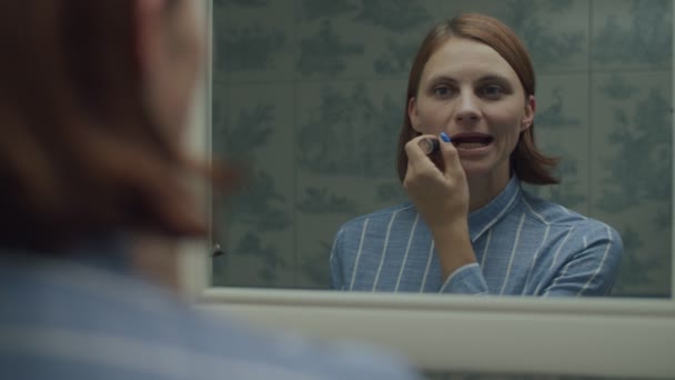 Jonge vrouwelijke volwassene in shirt aanbrengen make-up in spiegel reflectie in slow motion. Vrouwen zetten lippenstift in provence badkamer. — Stockvideo