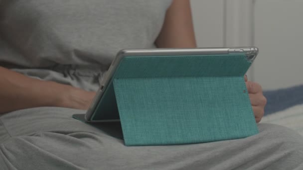 Nahaufnahme weiblicher Hände, die den Bildschirm eines Tablet-Computers in blauer Hülle berühren. Frauen sitzen mit Gadget im Bett — Stockvideo