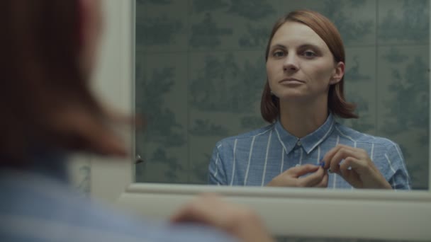 Jeune femme adulte en chemise se maquillant en miroir réfléchissant au ralenti. Femmes portant des boucles d'oreilles et souriant — Video