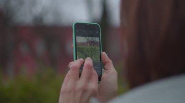Sonbahar parkında akıllı telefonuyla şehir görüşünün fotoğrafını çeken kadın ellerine yakın çekim. Üniversitenin fotoğrafını çeken kadın turist. 