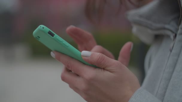 Close-up van de vrouw handen surfen online in smartphone in slow motion. Vrouwelijke vingers aanraken telefoon scherm met wazig stad achtergrond. — Stockvideo