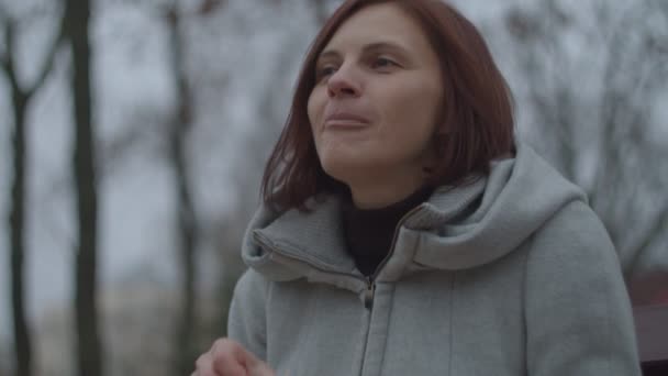 Junge brünette Frau schält Mandarinen auf Bank im Herbst Park. Weibchen mit umweltfreundlicher Tasche mit Mandarinen lächeln beim Mandarinenessen. — Stockvideo